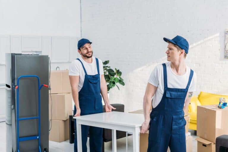 Zwei Umzugshelfer tragen einen Tisch aus einer Wohnung